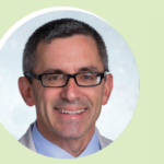 A middle-aged man with short dark hair, glasses, and a light blue collared shirt smiles at the camera against a light background with a pale green border.