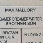 A memorial brick reads: "Max Mallory. Gamer Dreamer Writer Brother Son" in bold black letters on a light-colored background, set in a wall with other engraved bricks.