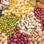 A colorful assortment of various dried beans and lentils arranged in sections, including black beans, chickpeas, green mung beans, red beans, split peas, lima beans, and speckled pinto beans.