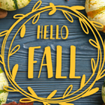 Yellow text reading "Hello Fall" in a decorative wreath overlay on a wooden surface, surrounded by green and yellow striped pumpkins, nuts, and autumn leaves.