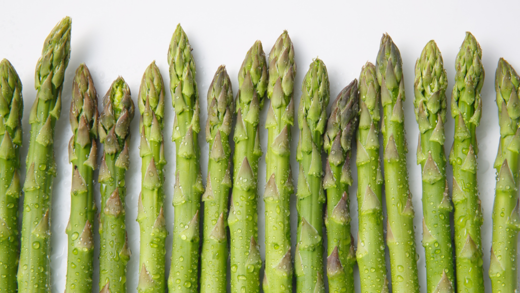 Fresh green asparagus spears arranged side by side on a white background, with droplets of water visible on the stalks.