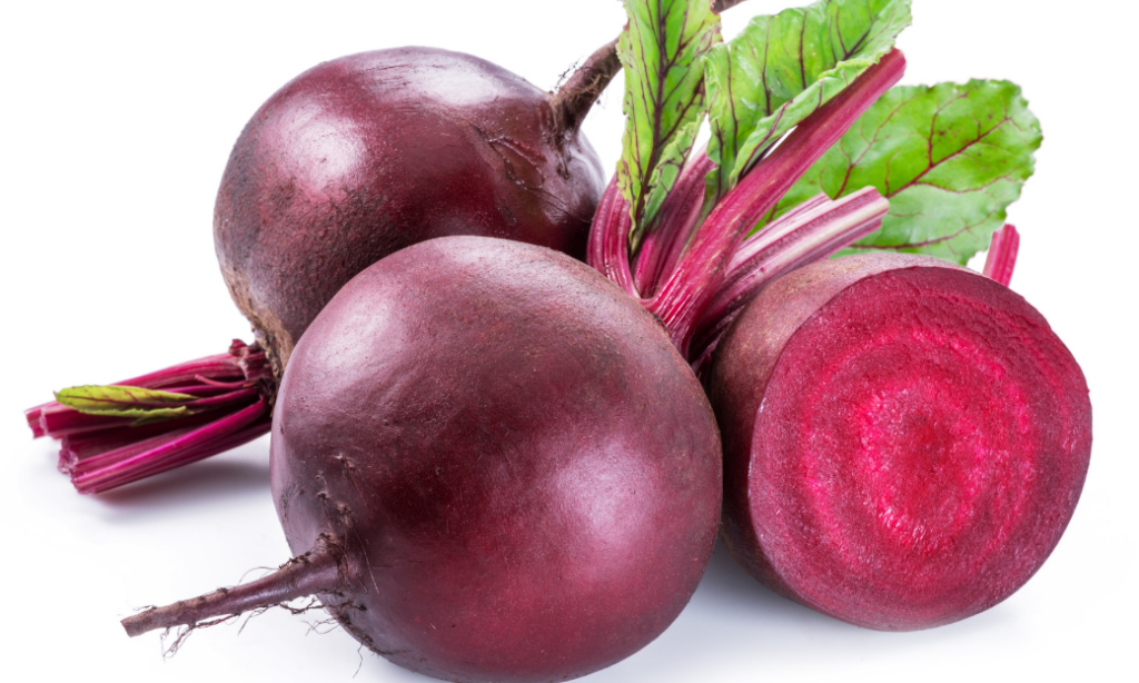Three fresh beetroots with stems and leaves, one of which is sliced in half to reveal its vibrant red interior, displayed on a white background.