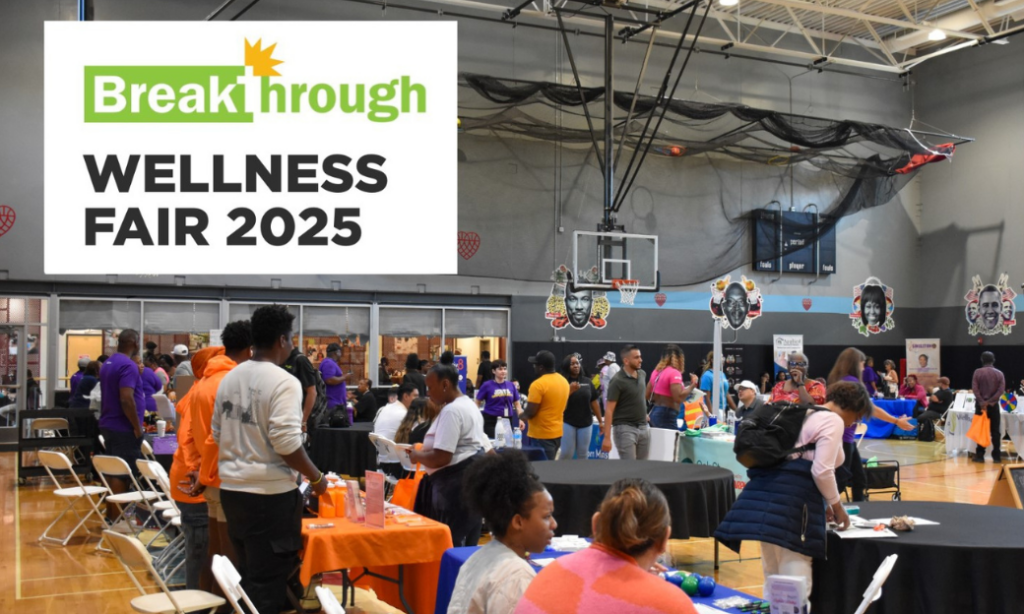 A busy gymnasium hosts the Breakthrough Wellness Fair 2025, with people visiting tables, speaking with vendors, and collecting information under a large sign announcing the event.