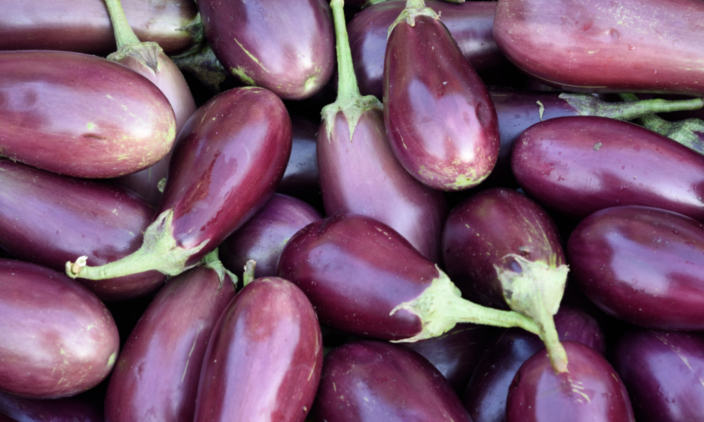 A close-up of several fresh, purple eggplants with green stems, piled together.
