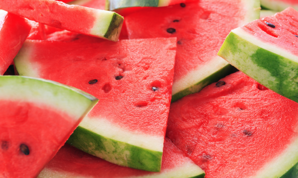 Sliced watermelon pieces with bright red flesh, black seeds, and green rind, stacked closely together in a vibrant, fresh display.