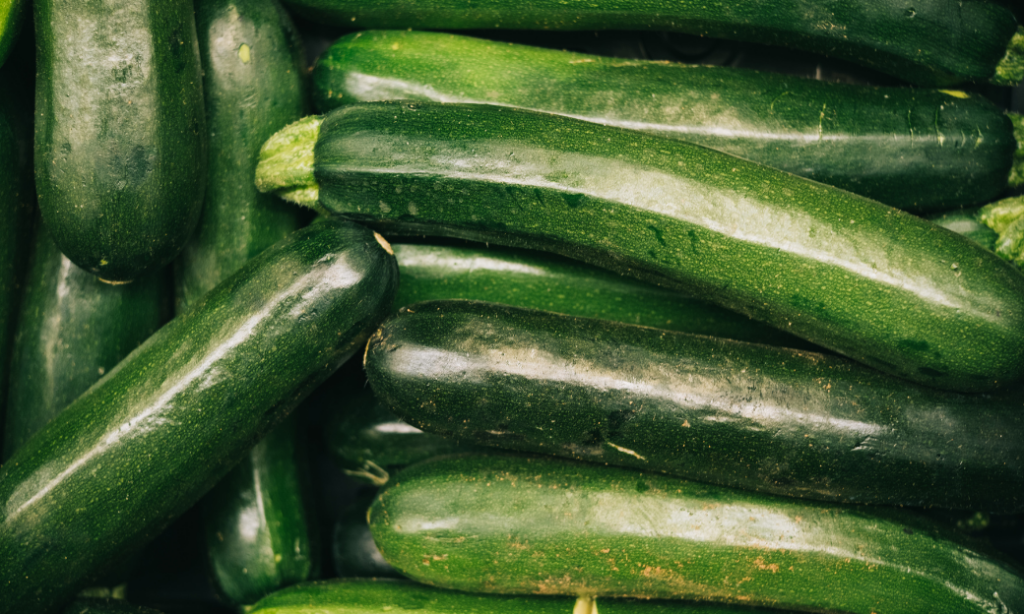 A close-up of several fresh zucchinis stacked together, displaying their glossy, dark green skin.