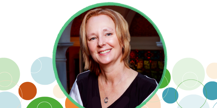 A woman with short blonde hair smiles at the camera, wearing a black and white top and a necklace. The photo is framed in a green circle with colorful overlapping circles in the background.